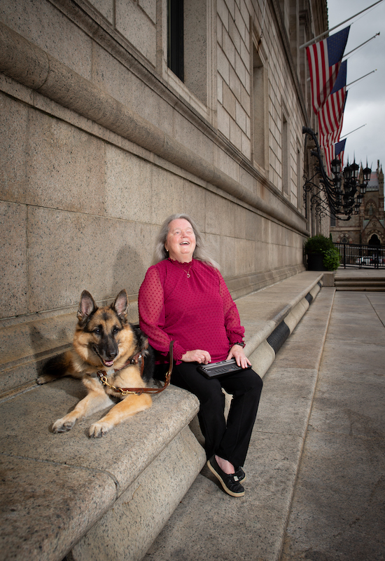 Judith Dixon outdoors in front of the Boston Public Library with her German shepherd guide dog, Potter